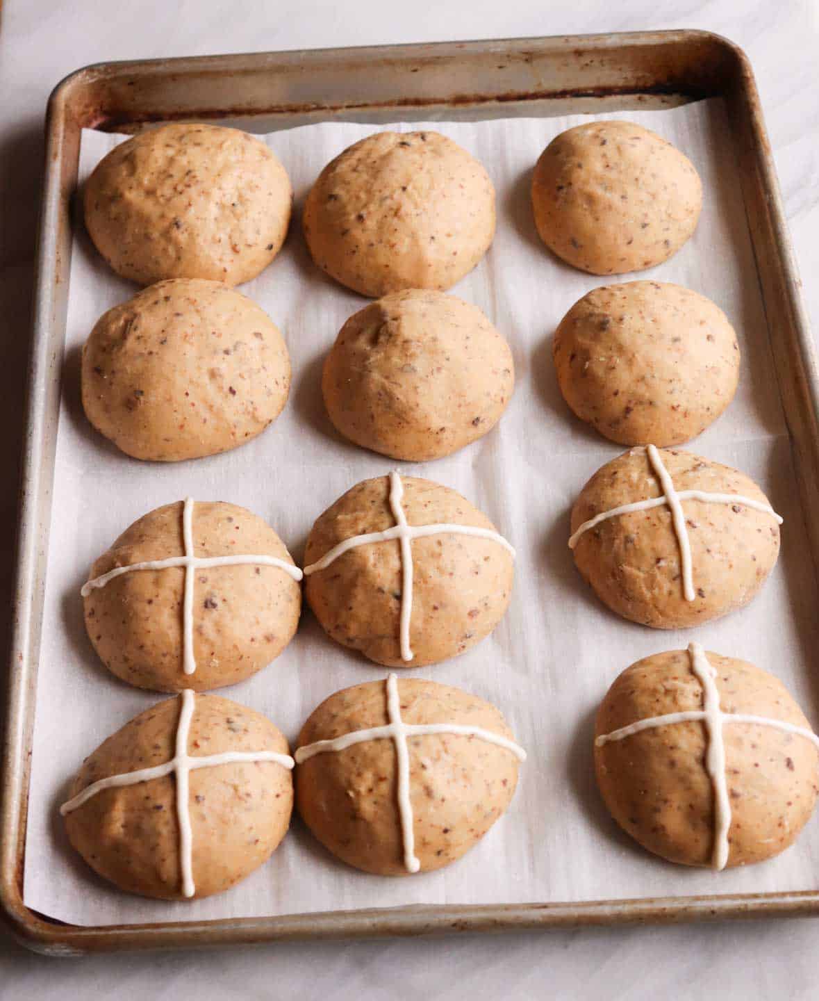 dough buns with a cross on a baking pan ready to be baked