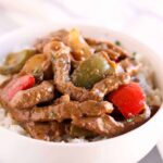 Pepper steak on top of rice in a bowl.