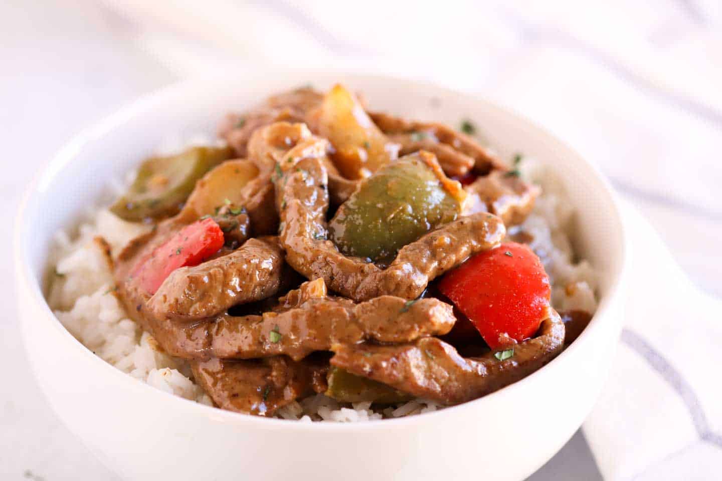 Pepper steak on top of rice in a bowl.