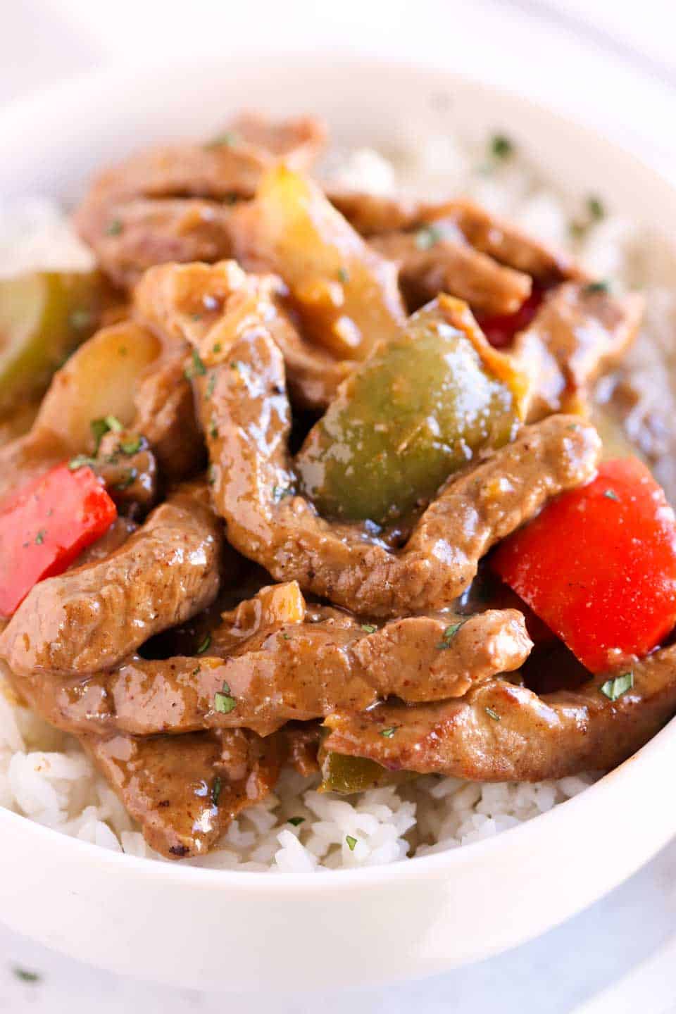 close up shot of strips of beef stir fried with red and green peppers on top of rice