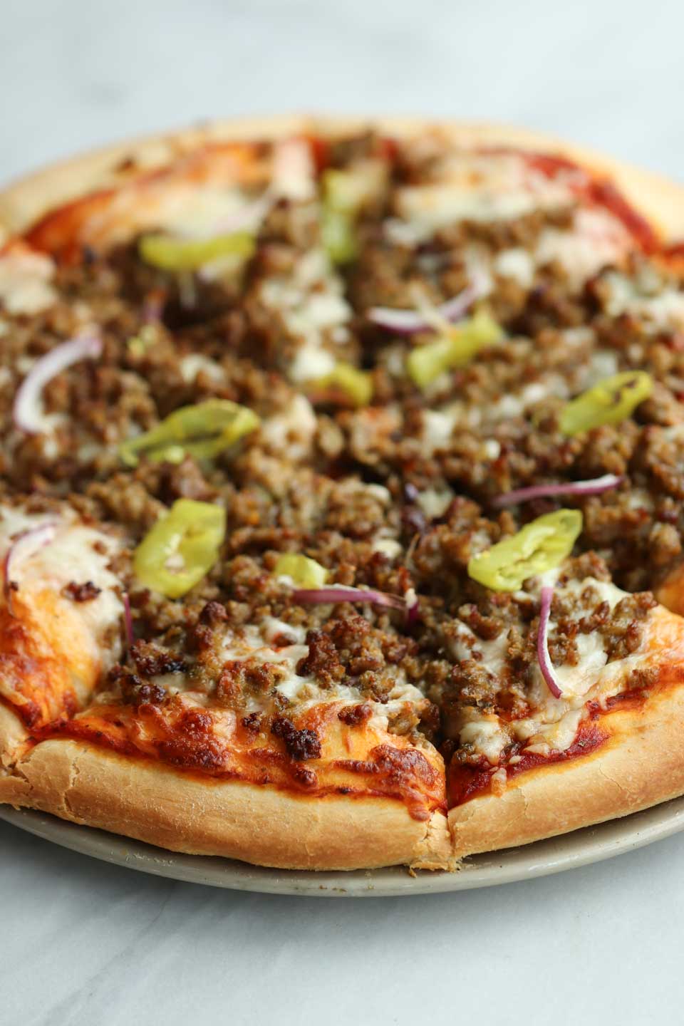 upclose shot of sausage pizza with red onions and pepperoncini 