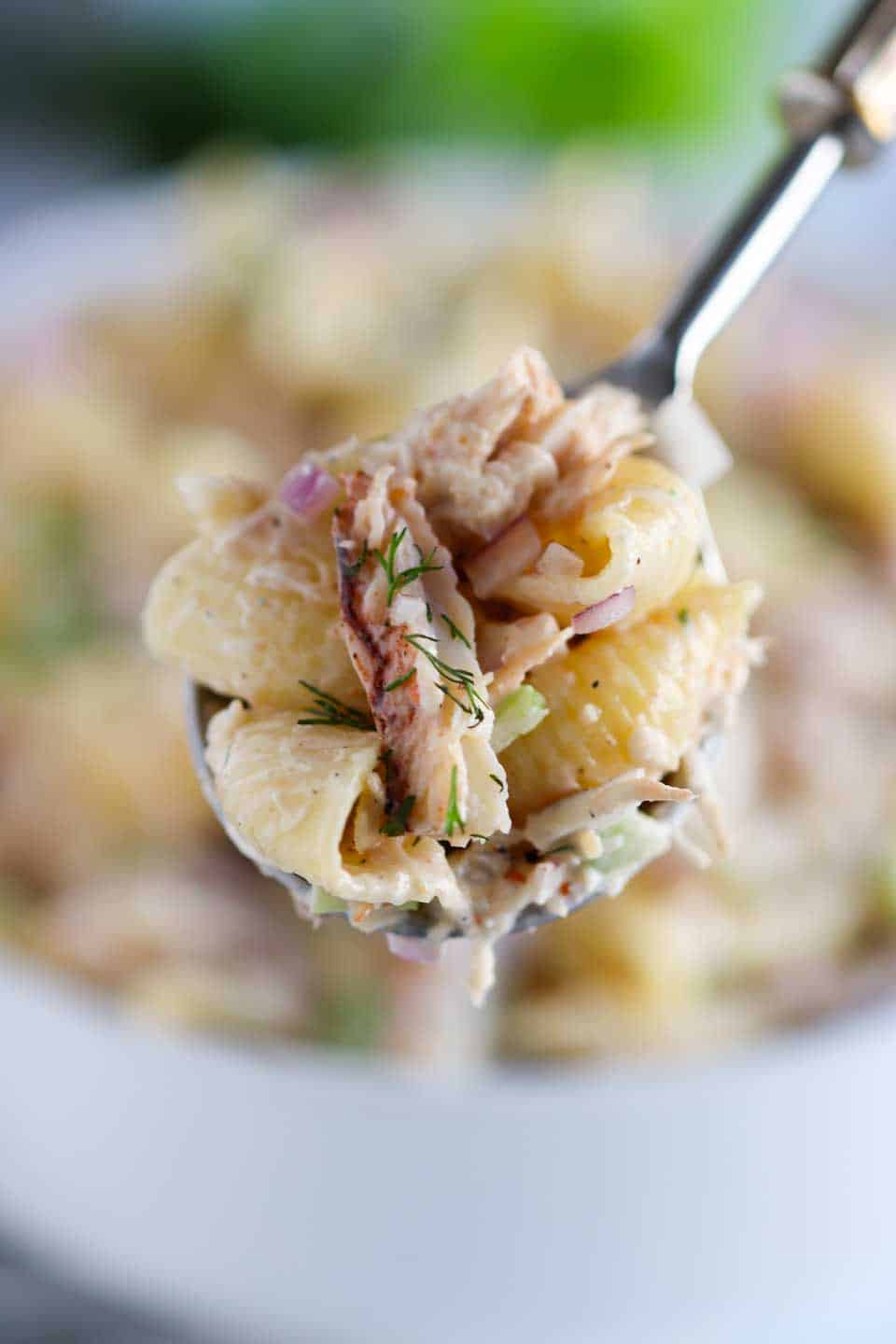 up close image of pasta salad with crab, herbs and onions on a spoon.