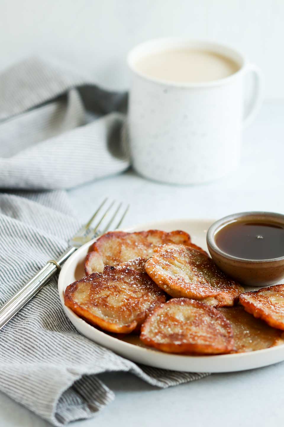 Jamaican banana fritters served on a plate with a small dish of maple syrup on the side. The fritters are golden brown and look crispy on the outside.